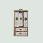 A wooden gift box containing various Marfuga Bio Cosmetics skincare products. The products are arranged neatly in wood wool and include body wash, nourishing oil, shampoo, hand and face cream. The box has a green rope handle.