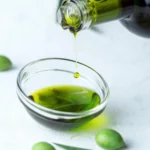 Fresh olives drizzling El Más Verde Novo extra virgin olive oil, highlighting its rich texture and color.