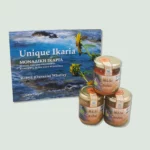 A display of the book "Unique Ikaria" by Robyn (Ourania) Whatley, alongside three jars of honey. The book cover features a scenic view of Ikaria with sunflowers, and the jars have labels indicating they are honey from Ikaria Greece.