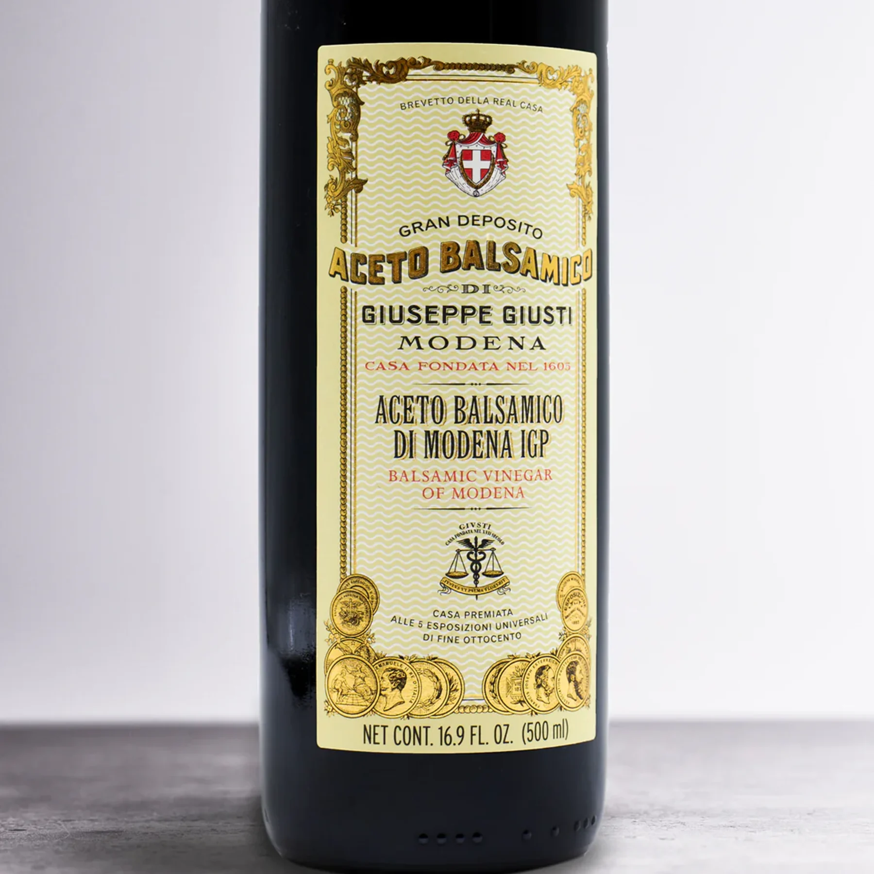 Giusti Balsamic Vinegar of Modena on a wooden kitchen counter next to fresh vegetables and bread.