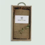 The inside of a Gourmet Groceries gift box, with products under a linen wrapping, a card, and an olive leaf.